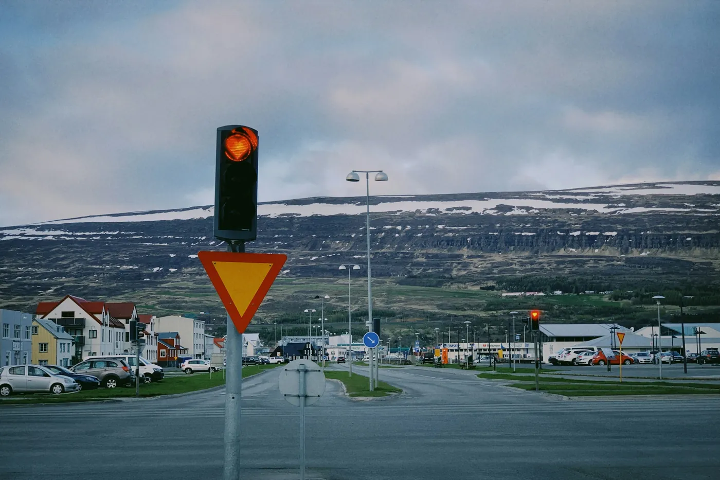 Carrefour à Akureyri avec un feu et un panneau de cédez-le-passage, des voitures garées et des maisons sous une longue crête de montagne