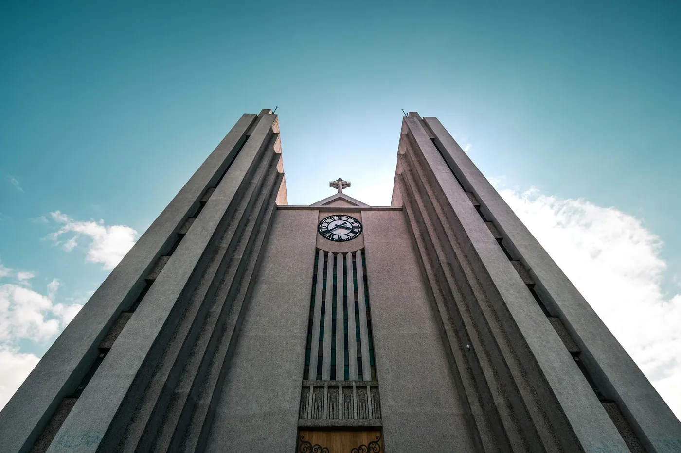 Low-angle view of a concrete church with two tall towers and a clock, blue sky