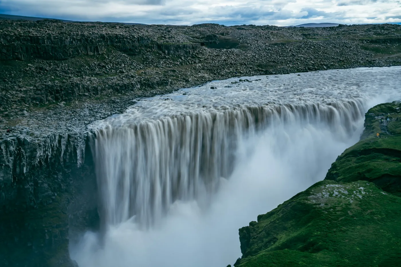 Cascata larga e potente che si getta in un canyon con spruzzi, pendio muschioso a destra