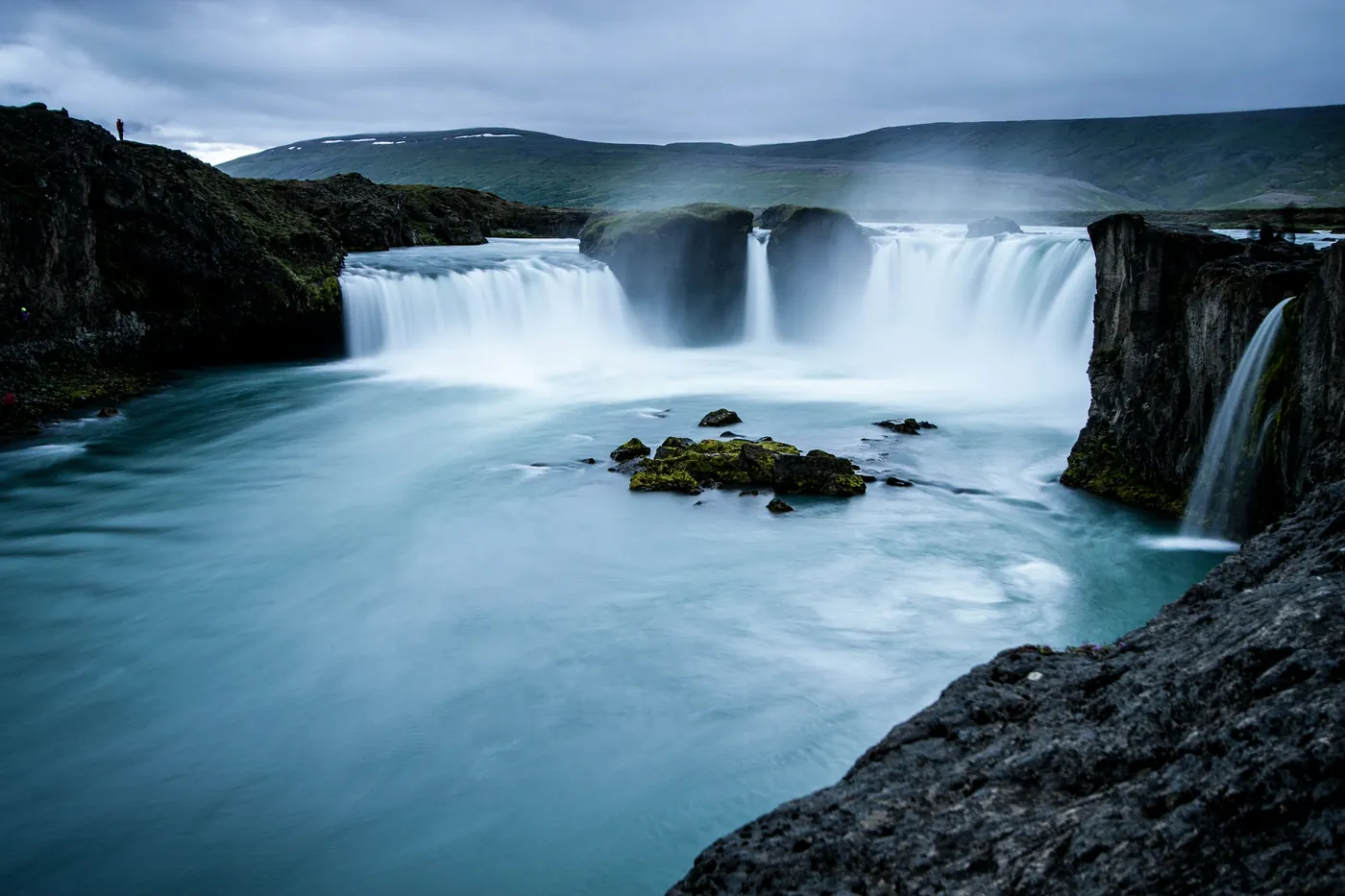 Horseshoe-shaped waterfall in long exposure, turquoise pool with a small mossy rock