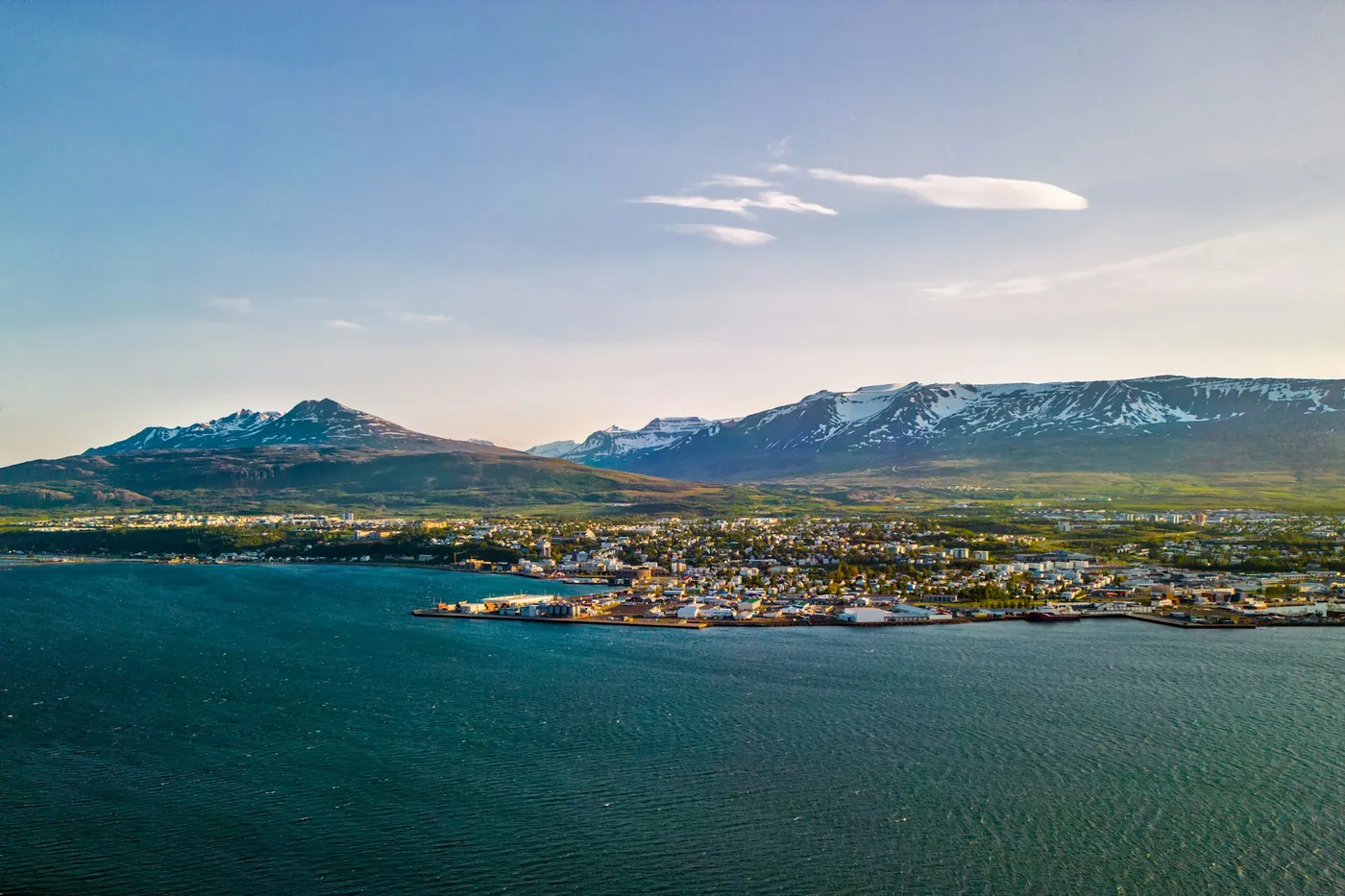 Akureyri seen across the fjord in evening light, the town along the shore with snow-streaked mountains behind
