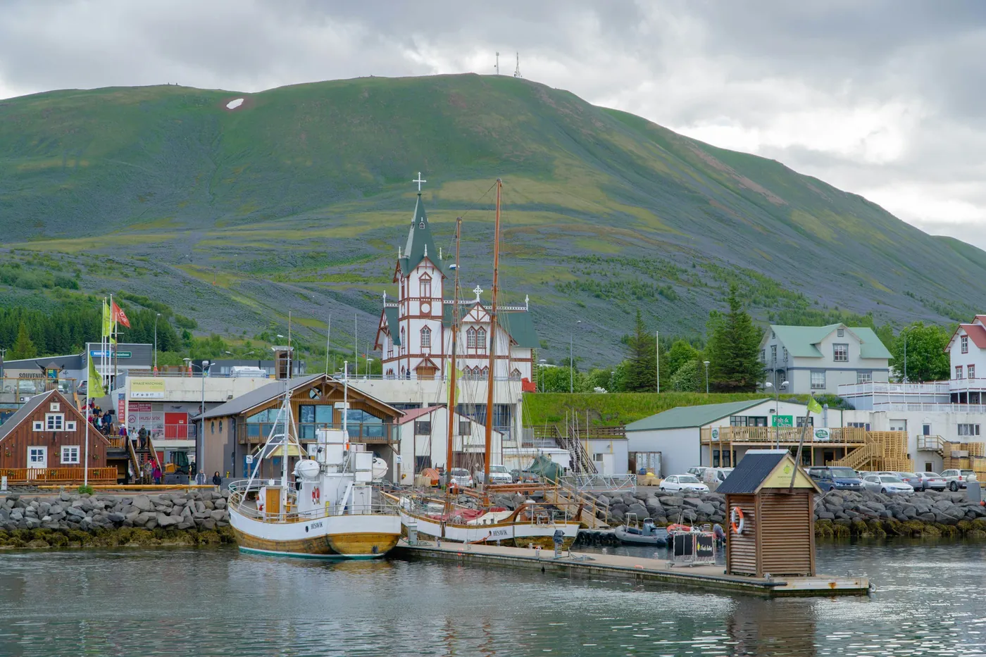 Húsavík harbour with boats and the white wooden church in front of a green mountain