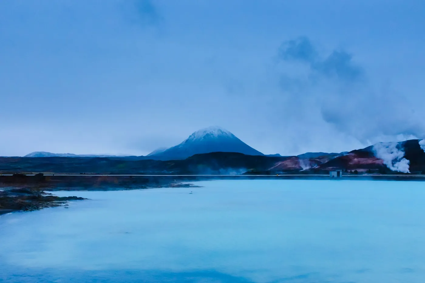 Milky blue geothermal water with steam and a snowy volcanic cone in the distance