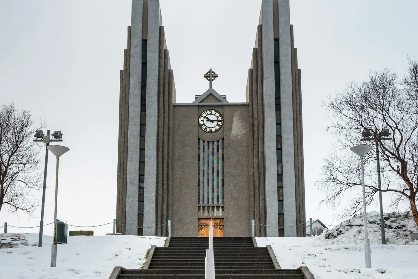Concrete church with twin towers at the top of a stairway, snow on the ground and bare trees