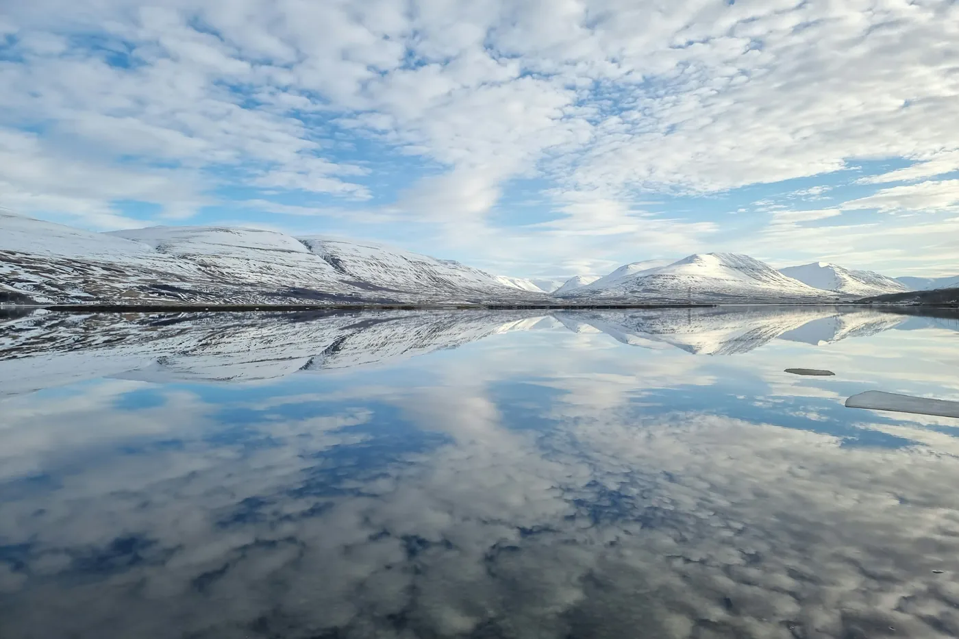Montagne innevate riflesse in un fiordo calmo sotto un cielo pieno di nuvole